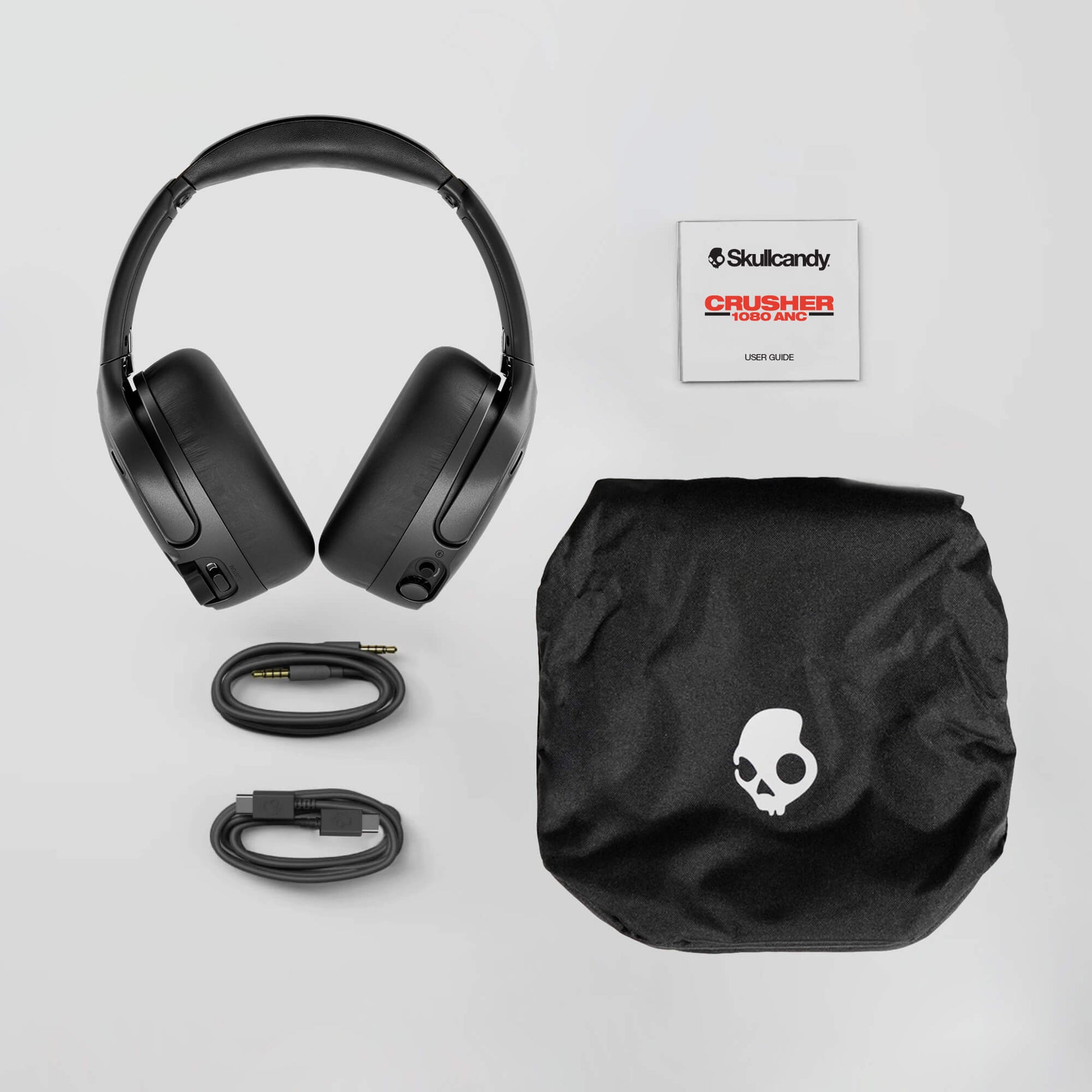 Black headphones with accessories and Skullcandy logo on a light gray background | Cement