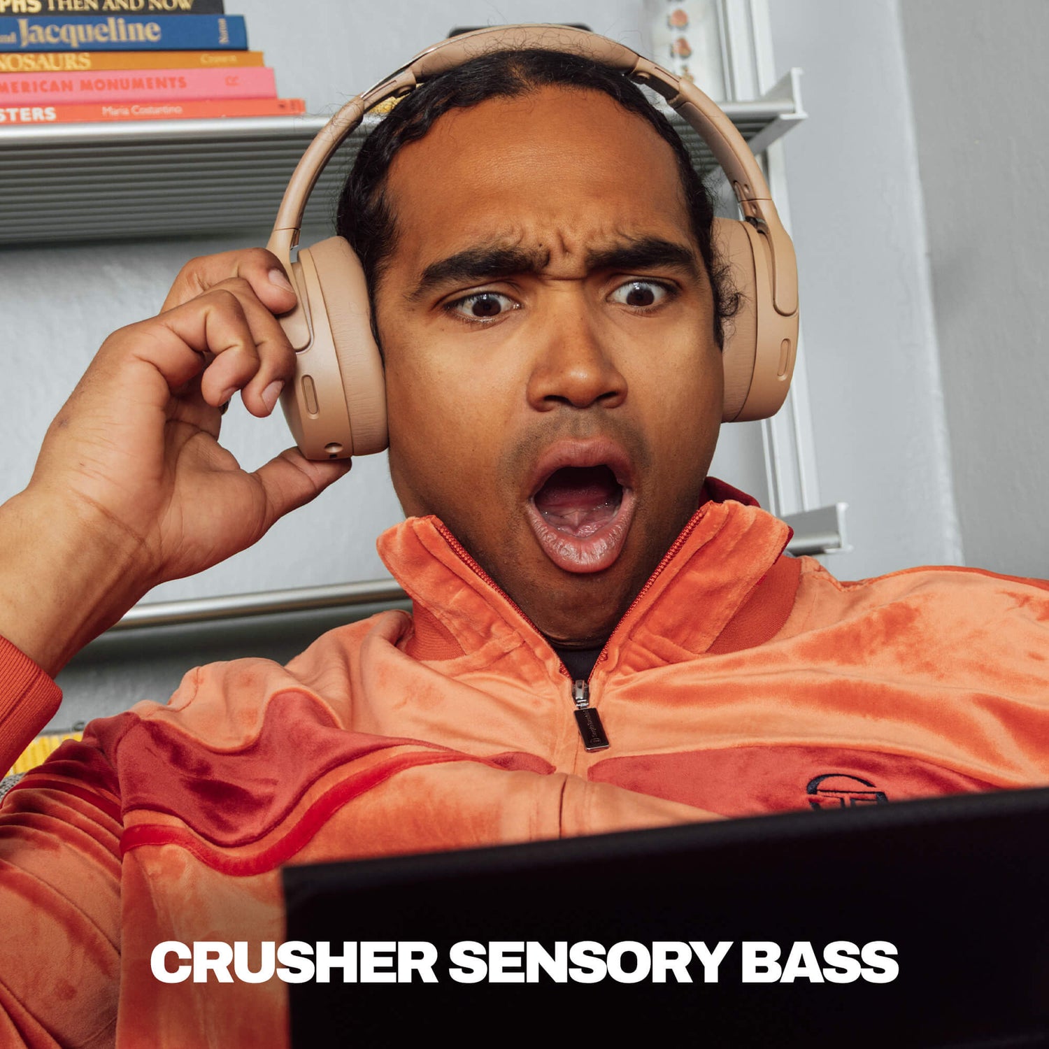 Person wearing Skullcandy Crusher 1080 ANC headphones with a surprised expression, sitting in front of a laptop with 'Crusher Sensory Bass' text. | Primer