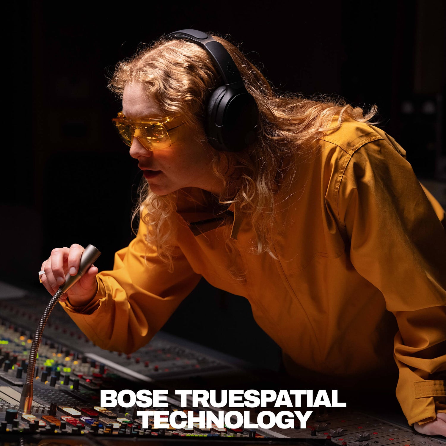 Person wearing headphones and sunglasses in front of audio equipment with 'Bose TrueSpacial Technology' text. | True Black