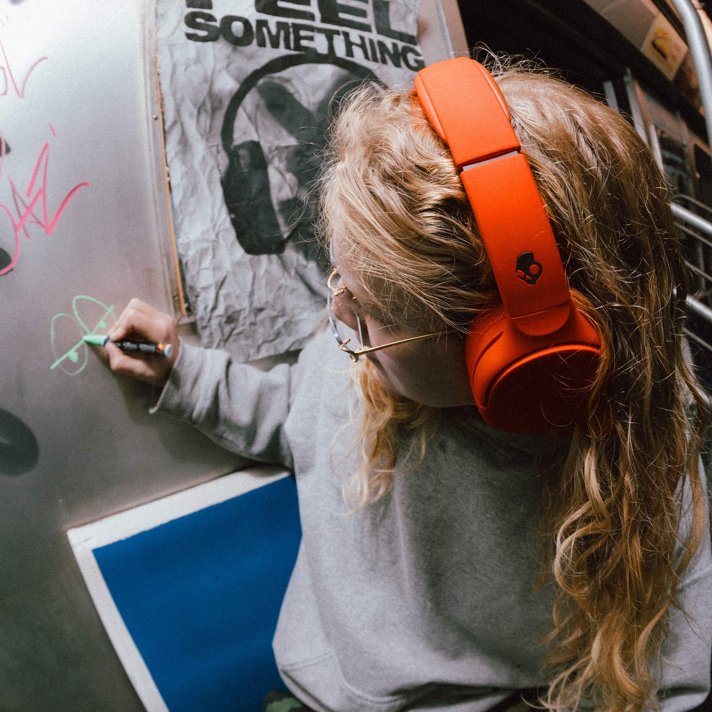 Person wearing orange Crusher 720 headphones writing on a whiteboard with a graphic design in the background. | Plasma