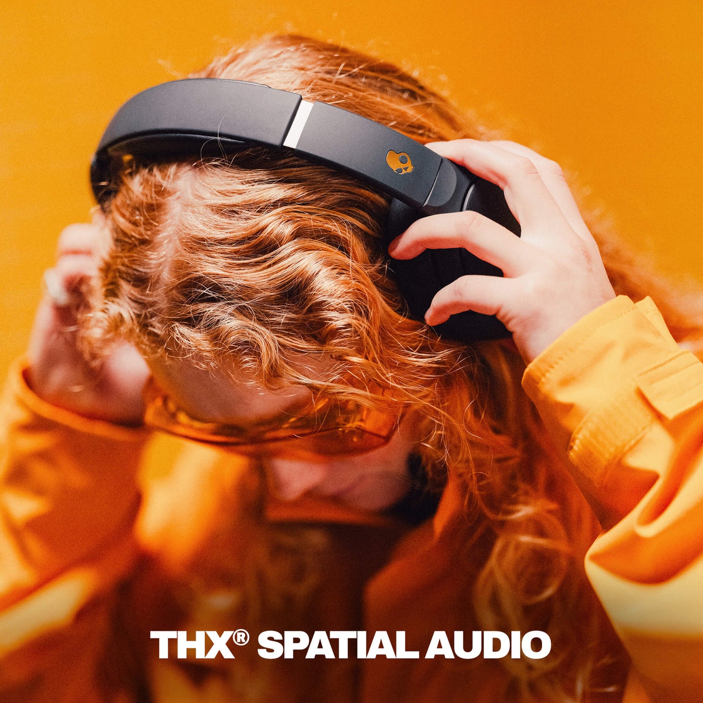 Person wearing black Crusher 720 headphones with THX Spatial Audio branding against an orange background | True Black