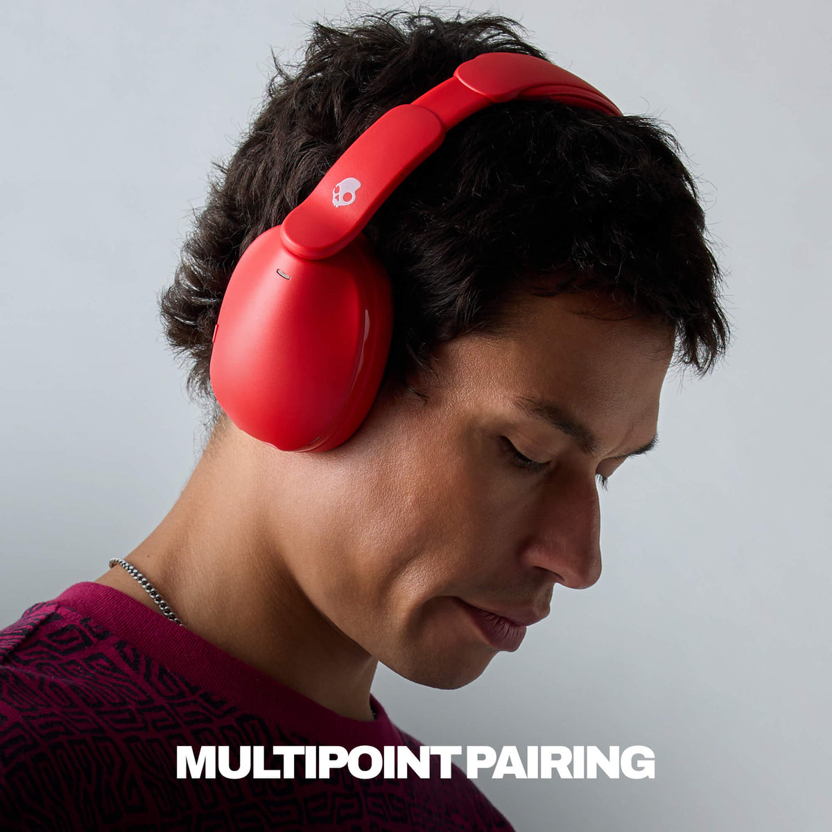 A man wearing bright red hesh 360 over-ear headphones with a white logo on the headband, shown in profile against a light gray background. White text at the bottom reads 'MULTIPOINT PAIRING'. | Plasma