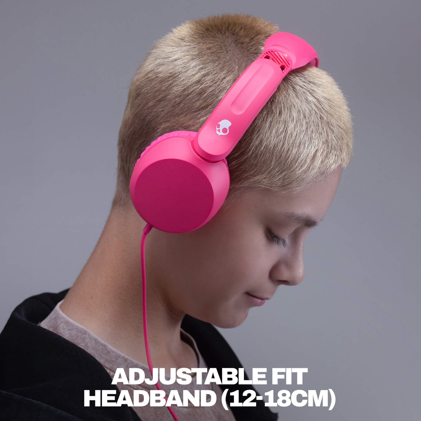 A person with short blonde hair wearing bright pink over-ear headphones with a visible pink cable, shown against a gray studio background with the text 'ADJUSTABLE FIT HEADBAND (12-18CM)' at the bottom. | Crazy Pink