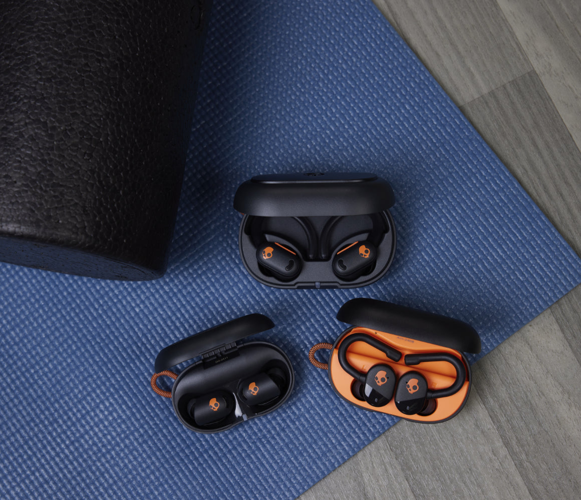 Skullcandy earbuds in a charging case next to a set of dumbbells in a gym
