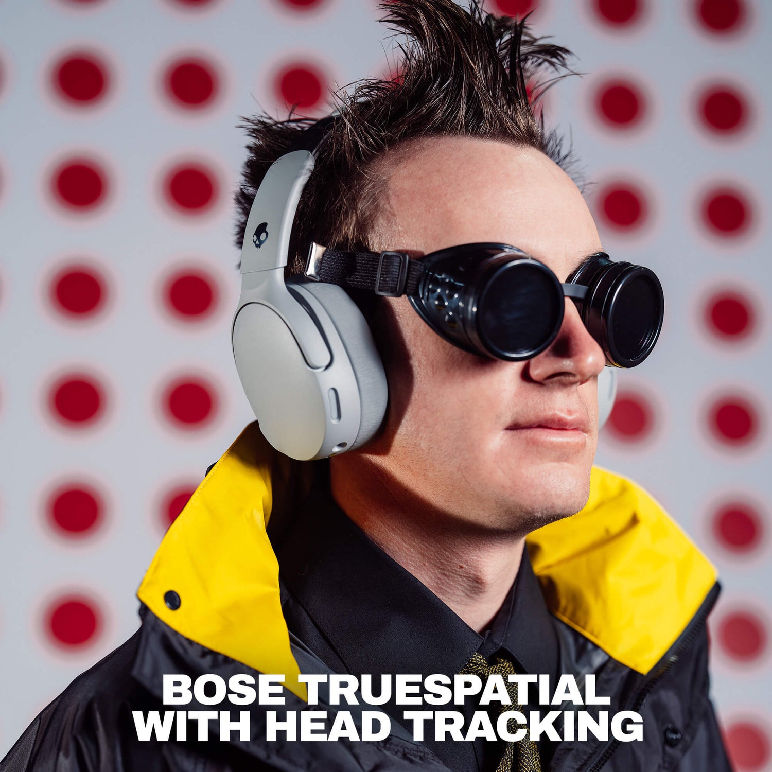 A man wearing white Crusher 1080 headphones with Bose TrueSpatial with black straps and round black goggles, set against a white background with red polka dots. Text at the bottom reads 'BOSE TRUESPATIAL WITH HEAD TRACKING'. | Cement